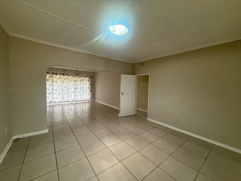 Spacious open-plan living area featuring neutral tiled flooring, a central skylight, and a classic archway connecting to an adjacent room.