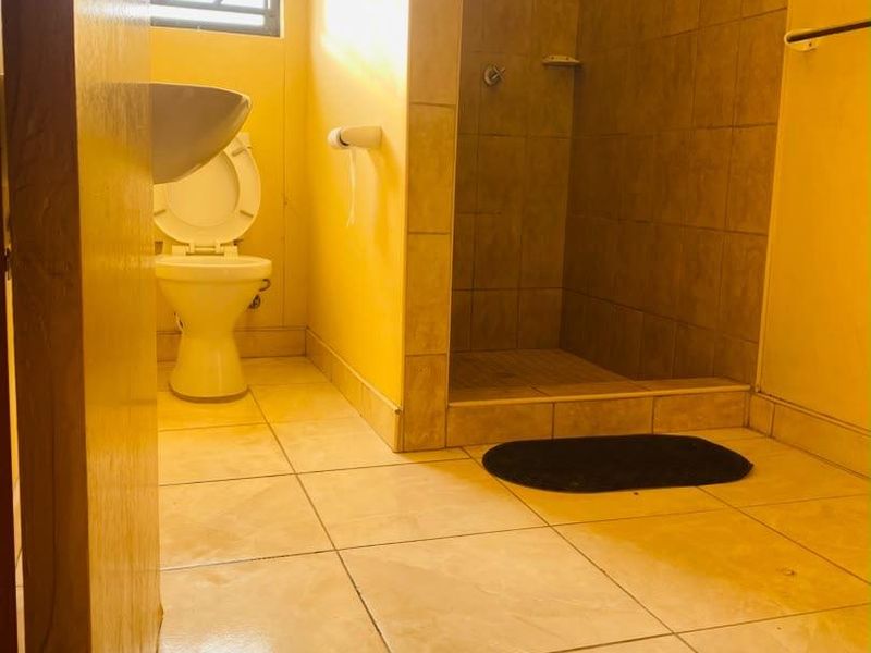 A functional bathroom featuring a walk-in shower, pedestal basin, and toilet, finished with neutral floor and wall tiling.