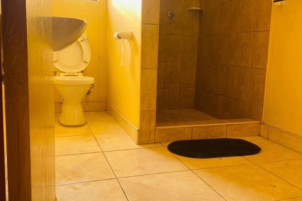 A functional bathroom featuring a walk-in shower, pedestal basin, and toilet, finished with neutral floor and wall tiling.