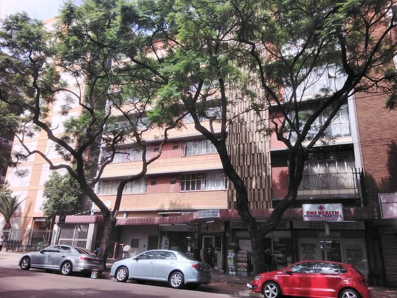 Street-level view of a multi-story apartment building featuring a brick facade, metal window frames, and ground-floor commercial retail spaces.
