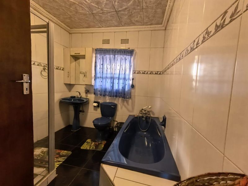 A dated bathroom featuring blue sanitaryware, a built-in bathtub, a separate shower enclosure, and tiled wall finishes.
