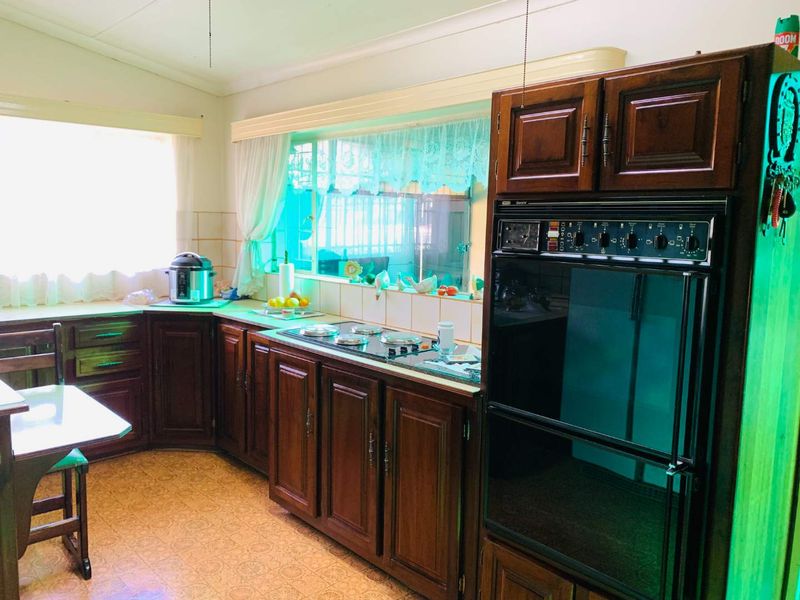 A traditional kitchen featuring dark wood cabinetry, a built-in wall oven, electric cooktop, and tiled backsplash with ample natural light.