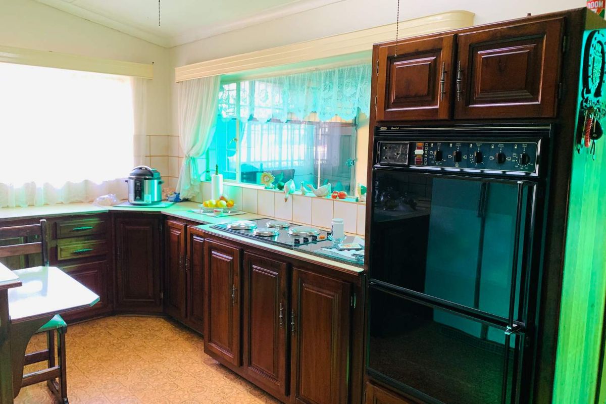 A traditional kitchen featuring dark wood cabinetry, a built-in wall oven, electric cooktop, and tiled backsplash with ample natural light.