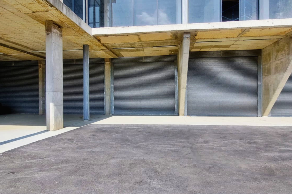 Industrial property featuring multiple secure roller shutter garage doors and a covered concrete parking area.