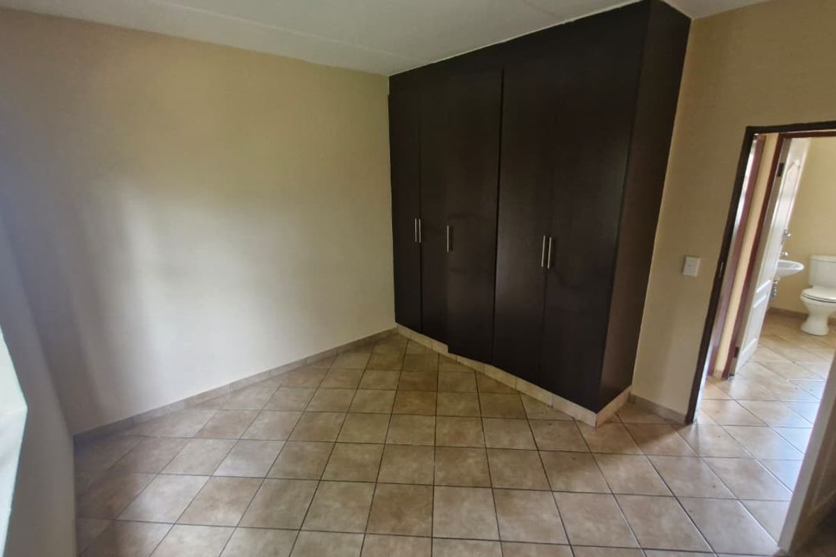 A bedroom featuring dark built-in cupboards, tiled flooring, and an adjacent bathroom entrance.