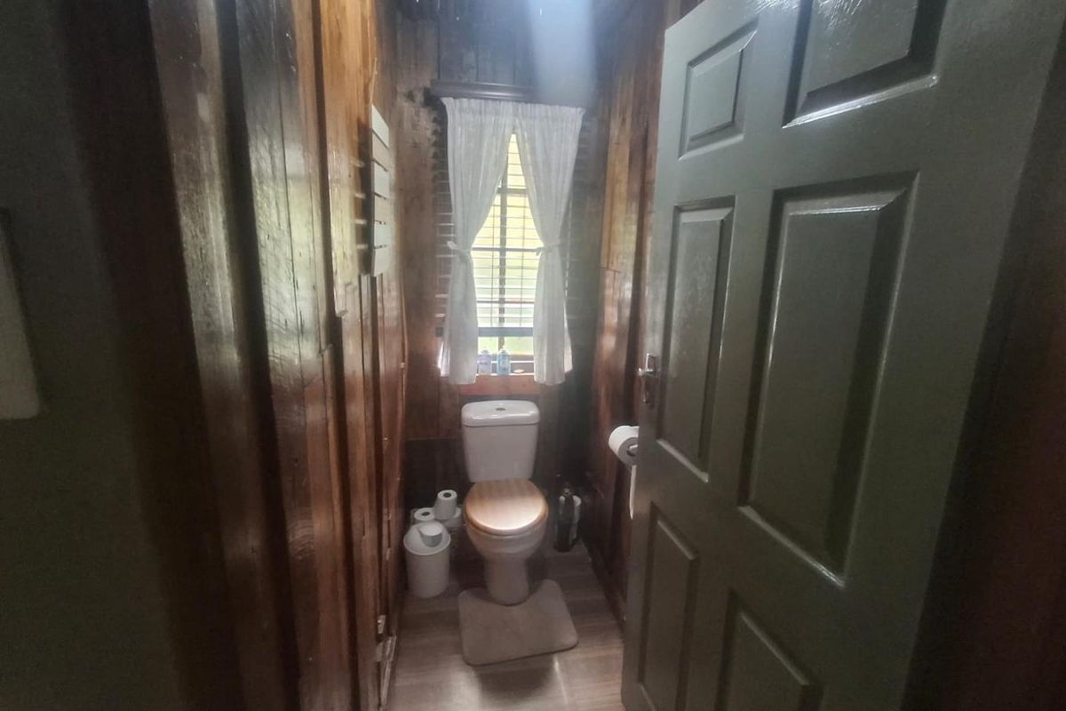 A compact bathroom featuring timber wall paneling, a standard toilet, and a window with natural light.