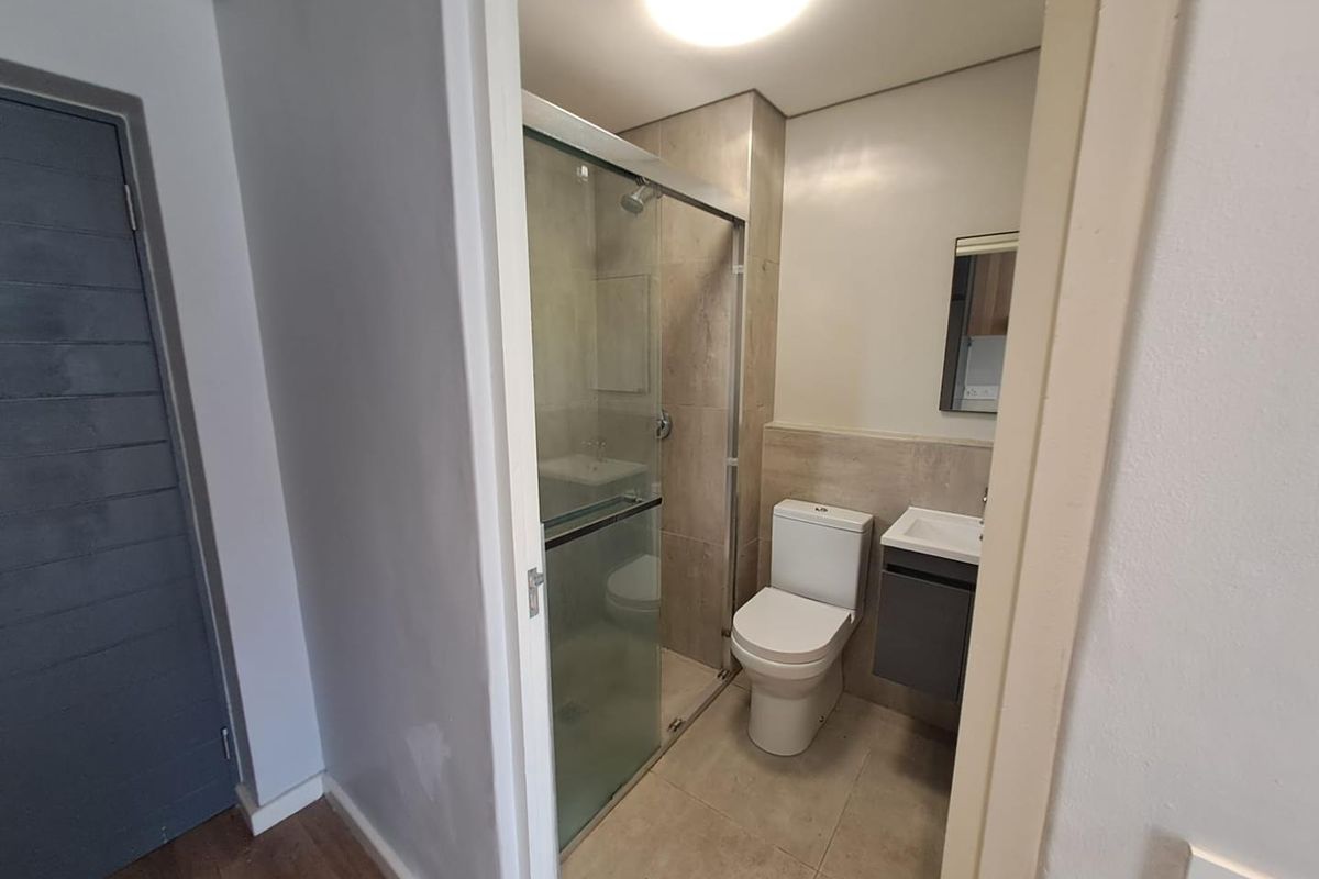 A modern, compact bathroom featuring a glass-enclosed shower, a wall-mounted vanity with a basin, and neutral floor-to-ceiling tiling.