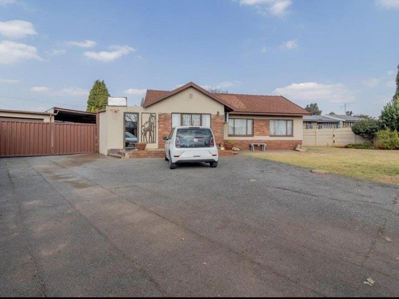 Front view of a single-story residential house featuring a tiled roof, brick facade, and a spacious asphalt driveway with perimeter fencing.