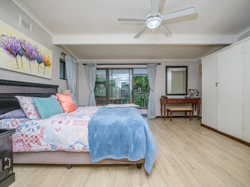 Spacious bedroom featuring light-toned laminate flooring, a ceiling fan, built-in wardrobe, and sliding glass doors providing access to an outdoor balcony area.