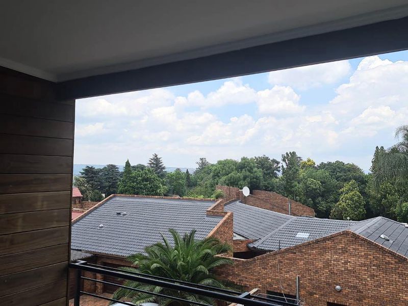 A covered balcony featuring a metal railing and timber-look wall cladding, offering an elevated view over the surrounding residential complex and greenery.