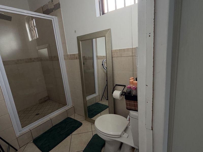 A functional bathroom featuring a shower enclosure, pedestal basin, and toilet, with ceramic tiling and unfinished wall sections requiring cosmetic attention.