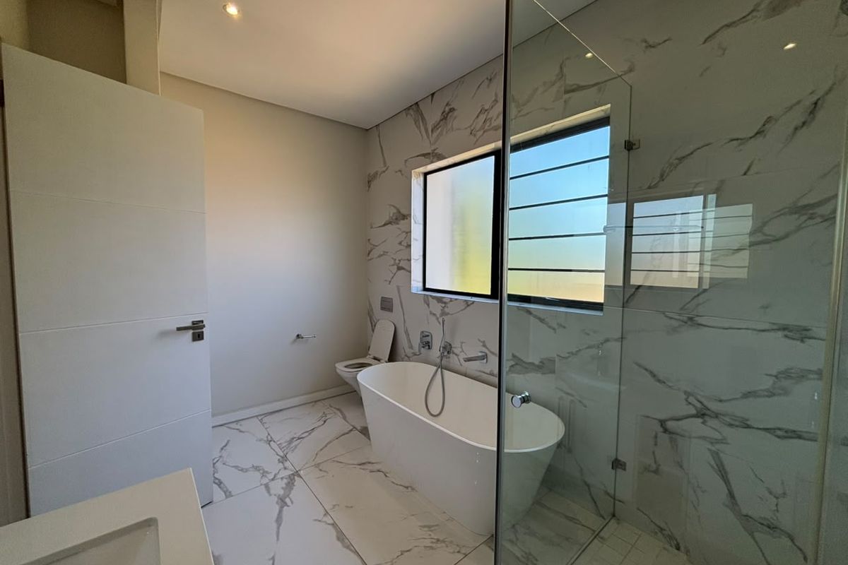 Modern bathroom featuring a freestanding bathtub, glass shower enclosure, and elegant marble-look tiling throughout.