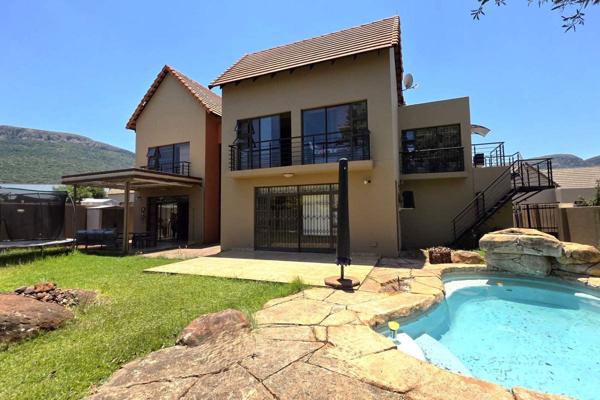 Rear view of a two-story house featuring a swimming pool with rock surround, a patio area, and upper-level balconies with metal railings.
