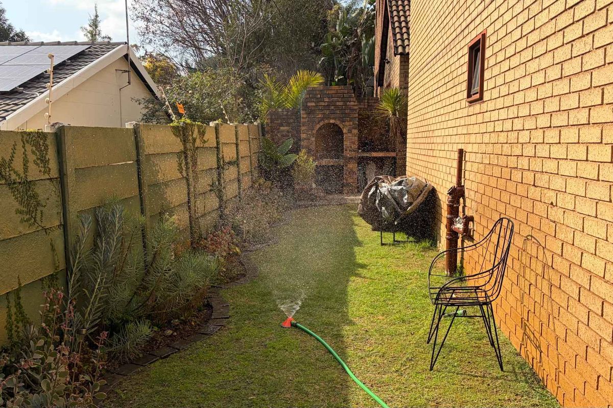 A side garden area featuring a brick boundary wall, a built-in brick braai, and a lawn area with irrigation.