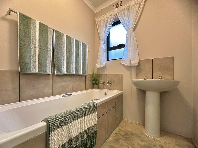 A functional bathroom featuring a bathtub with tiled surround, a pedestal basin, and a window for natural light.