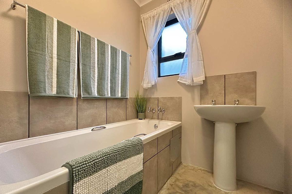 A functional bathroom featuring a bathtub with tiled surround, a pedestal basin, and a window for natural light.