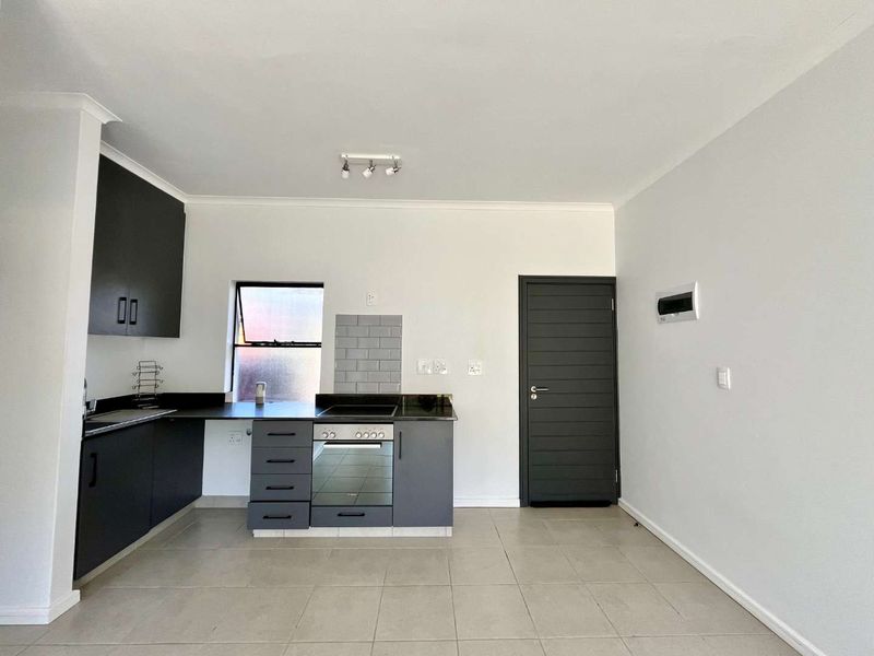 Modern kitchen featuring dark grey cabinetry, built-in oven and hob, subway tile backsplash, and neutral tiled flooring in an open-plan layout.