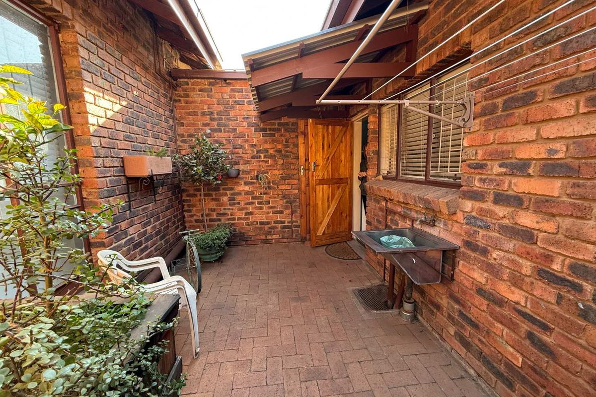A functional rear courtyard featuring exposed brick walls, brick paving, a utility sink, and a wall-mounted washing line under a covered awning.