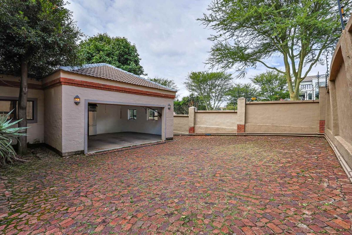 A spacious paved courtyard area featuring a detached garage structure with a tiled roof and perimeter boundary walls.