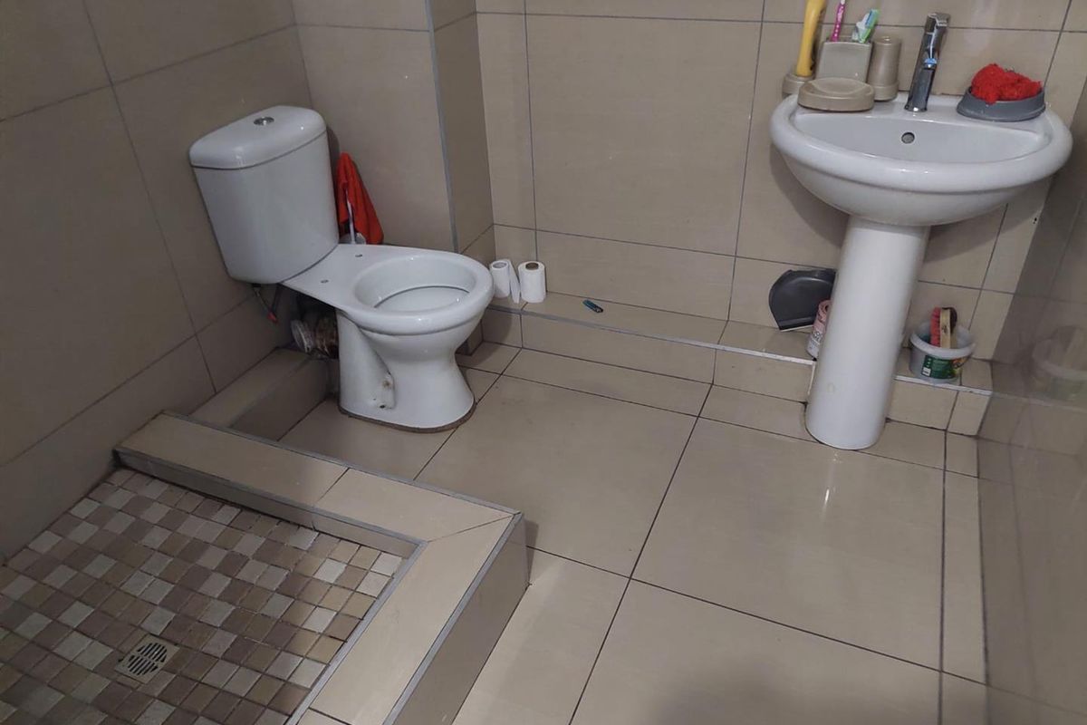 A functional bathroom featuring a pedestal basin, toilet, and a tiled shower base with neutral ceramic wall and floor tiling.