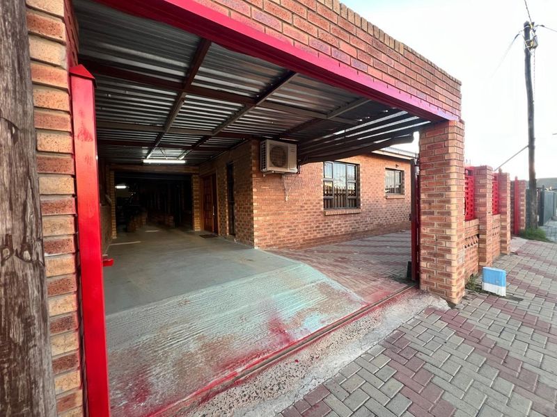 A brick-built garage with a corrugated metal roof, concrete driveway, and security bars on the windows, providing secure off-street parking.