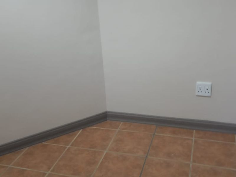 A clean, empty office corner featuring neutral wall paint, ceramic tile flooring, and installed skirting boards with an accessible electrical outlet.