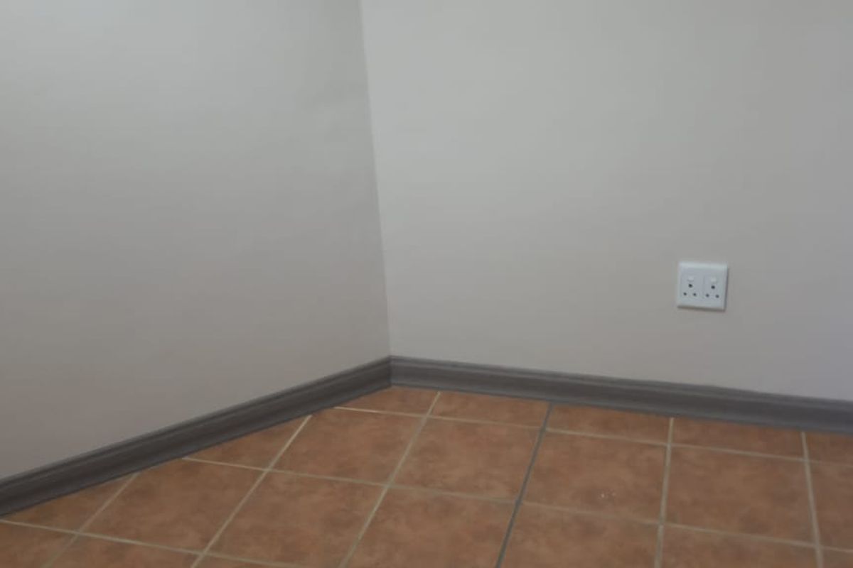 A clean, empty office corner featuring neutral wall paint, ceramic tile flooring, and installed skirting boards with an accessible electrical outlet.