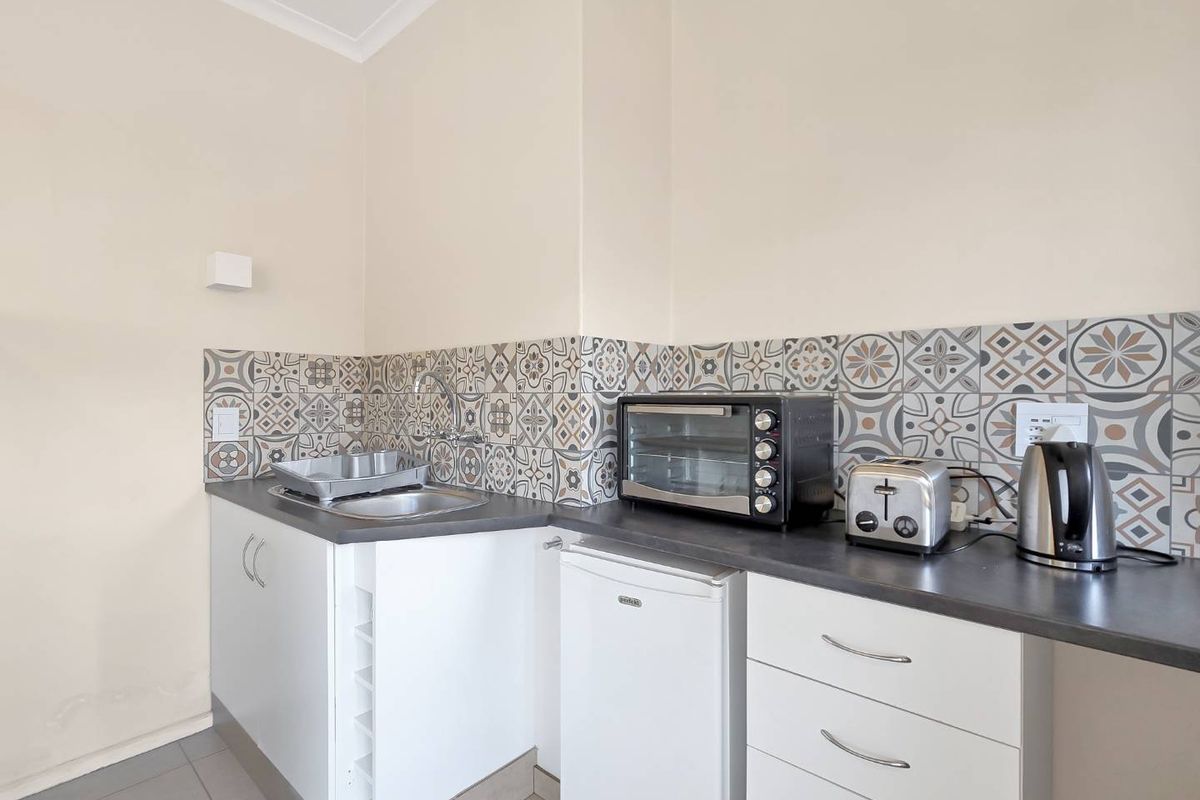 A compact kitchen area featuring white cabinetry, dark laminate countertops, and a decorative patterned tile splashback.