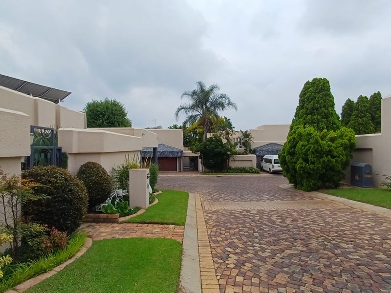 A view of the cluster property entrance featuring a paved driveway, landscaped garden areas, and residential building facades with solar panels.