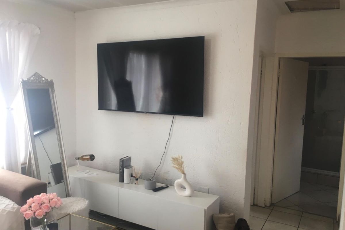 A living room area featuring a wall-mounted television and tiled flooring, with an adjacent doorway leading to a bathroom.