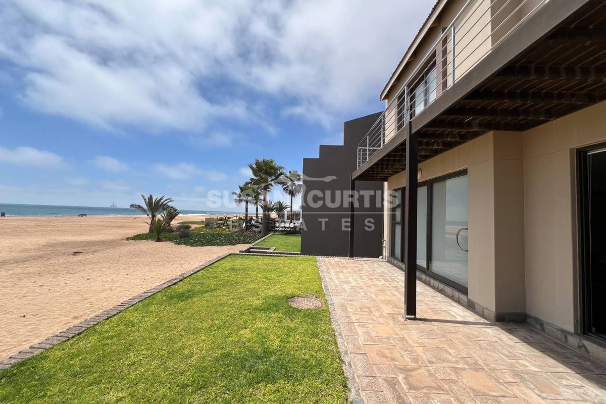 A view of the rear exterior of the townhouse, featuring a paved patio, manicured lawn, and direct access to the beach.