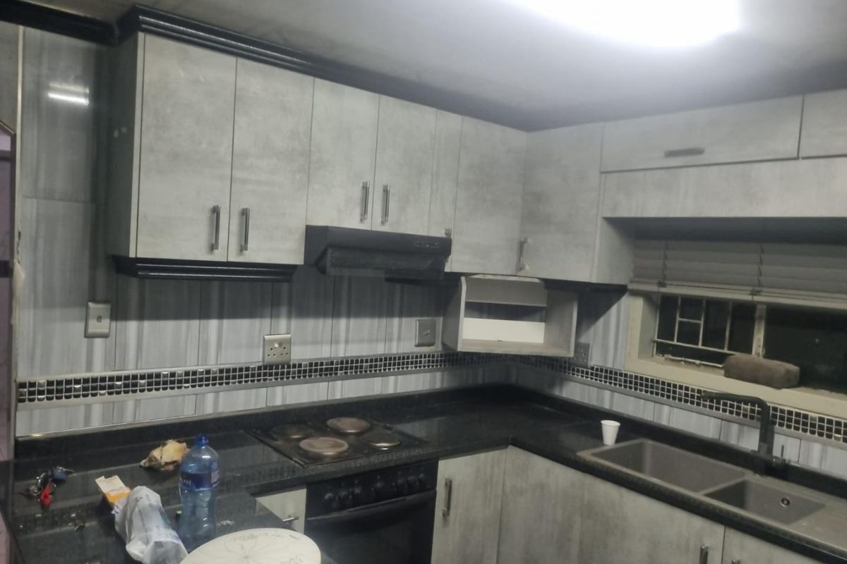 A functional kitchen featuring grey textured cabinetry, dark granite countertops, a built-in oven and hob, and a double basin sink.