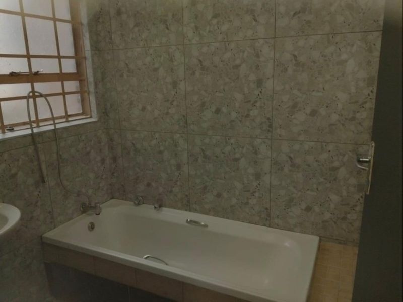 A functional bathroom featuring a built-in bathtub with mixer taps and neutral wall tiling, complemented by a window with security bars.