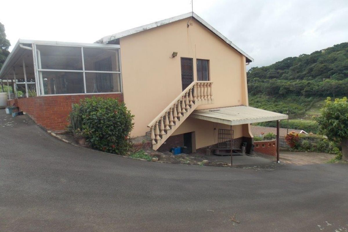 Rear view of the property featuring an enclosed patio, external staircase, carport, and paved driveway area set against a hillside backdrop.