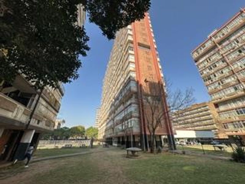 Exterior view of a multi-story apartment complex featuring a communal garden area and established residential surroundings.