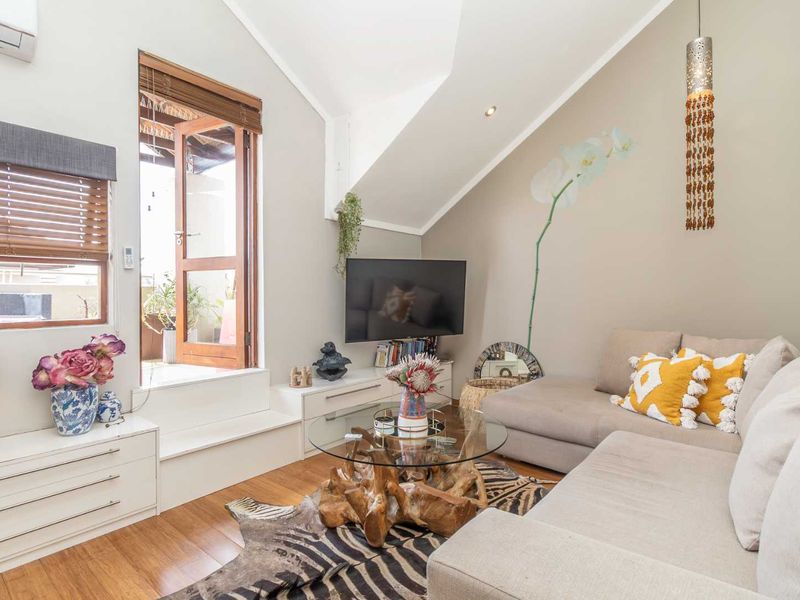A bright living room featuring vaulted ceilings, timber flooring, split-system air conditioning, and direct access to an outdoor balcony area.