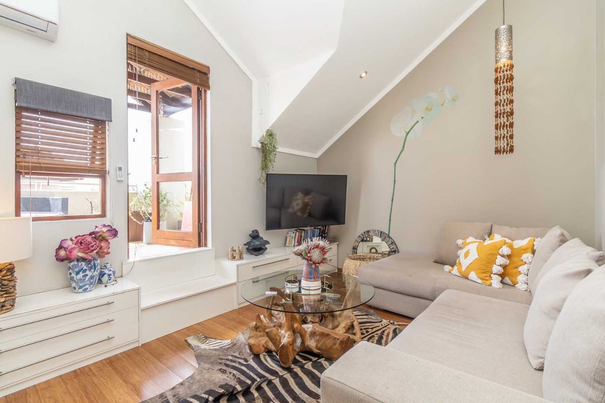 A bright living room featuring vaulted ceilings, timber flooring, split-system air conditioning, and direct access to an outdoor balcony area.