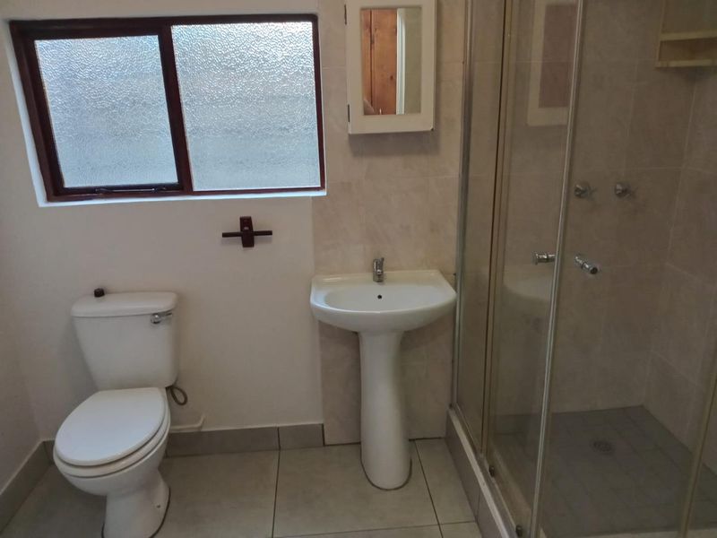 A functional bathroom featuring a pedestal basin, toilet, and a glass-enclosed shower with neutral wall and floor tiling.