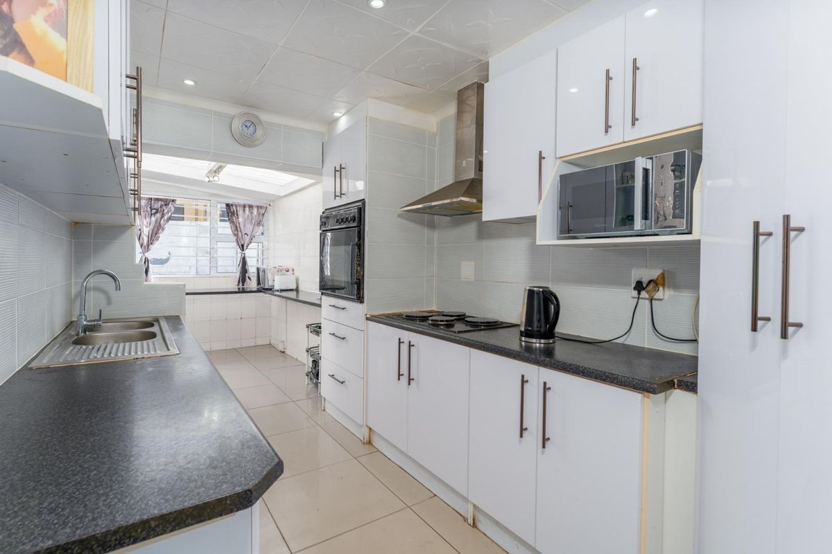A functional kitchen featuring white cabinetry, dark countertops, a built-in oven, hob, and extractor fan with tiled flooring.