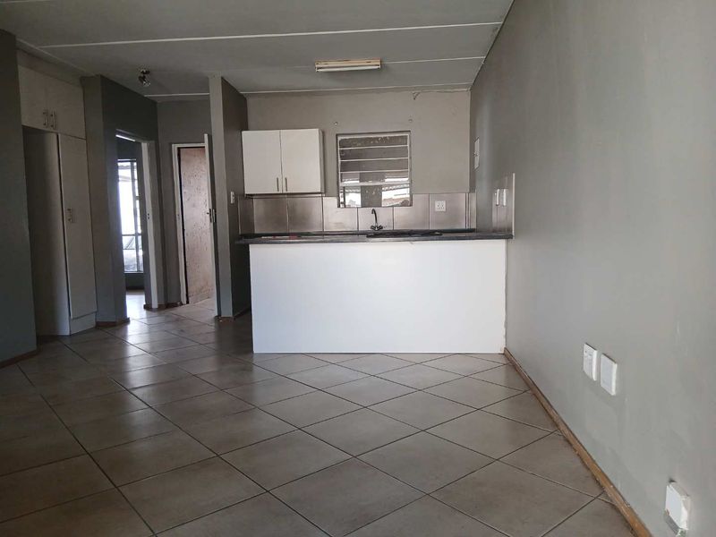 Open plan living and kitchen area featuring tiled flooring, built-in cabinetry, and a breakfast counter in a neutral, vacant space.