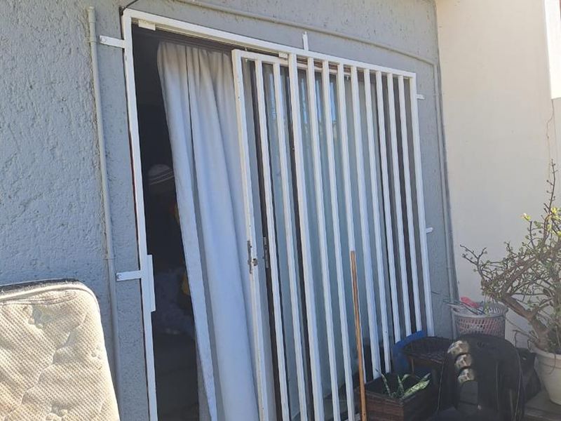 Exterior patio area featuring a security gate, sliding door access, and a wall-mounted air conditioning unit.