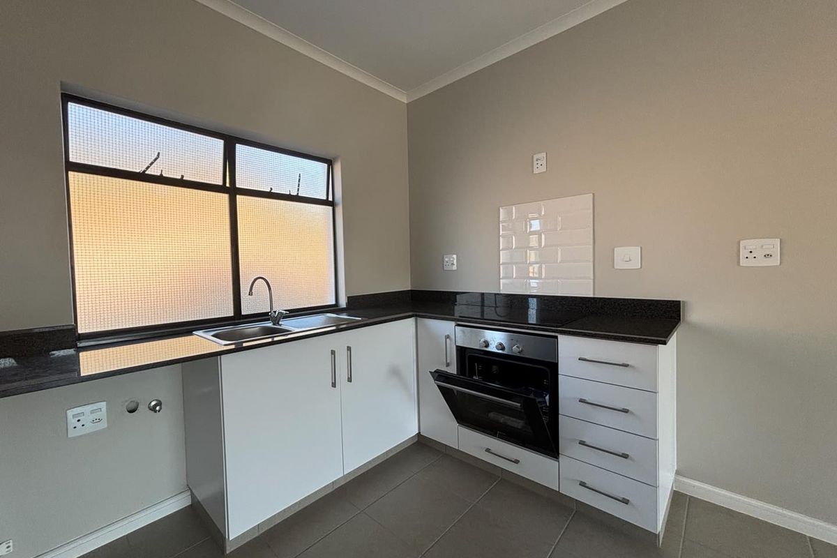 A clean, modern kitchen featuring white cabinetry, dark granite countertops, a built-in oven, and a stainless steel sink with tiled splashback.