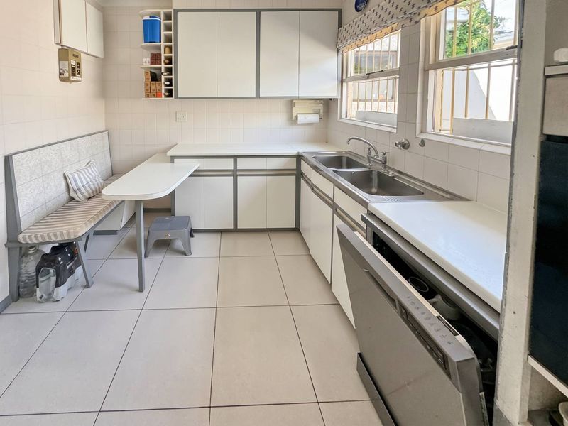A functional kitchen featuring white cabinetry, tiled splashbacks, double sink, and integrated dishwasher with a built-in breakfast nook area.