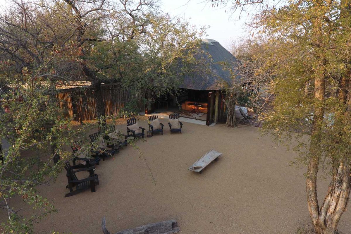 Aerial view of a bushveld property featuring a thatched-roof structure, open sandy courtyard, and mature trees in a natural setting.