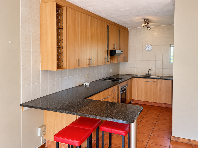 A functional kitchen featuring laminate cabinetry, granite countertops, a built-in oven and hob, and a breakfast bar with tiled flooring and backsplash.