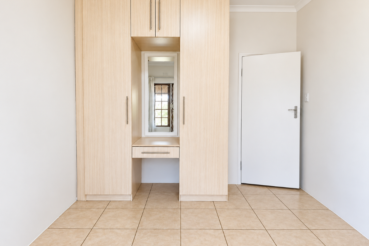 A clean, empty bedroom featuring light wood-toned built-in wardrobes with an integrated vanity and neutral tiled flooring.
