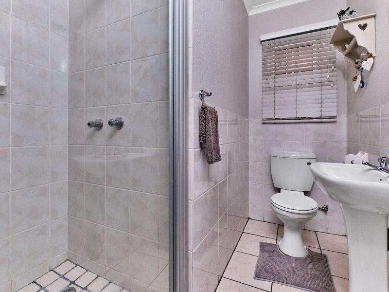 A functional bathroom featuring a tiled shower enclosure, pedestal basin, and toilet, finished with neutral wall tiles and practical window blinds.