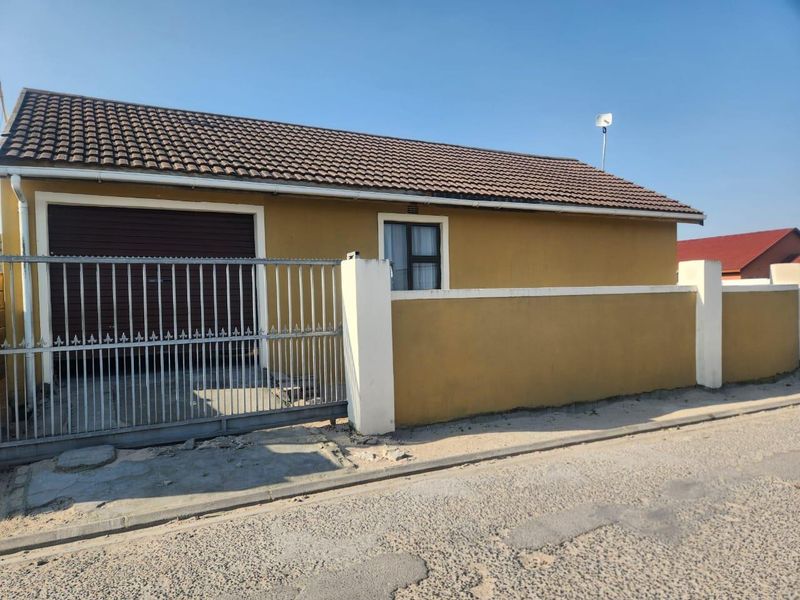 Front exterior view of the property featuring a tiled roof, roller garage door, and a secure perimeter wall with a metal sliding gate.