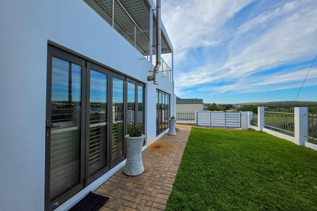 Rear exterior view featuring a paved walkway, manicured lawn, and modern aluminium stacker doors leading to the interior, with a balcony above.
