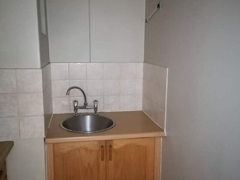 A functional scullery area featuring a stainless steel sink, laminate countertop, wooden cabinetry, and tiled backsplash.
